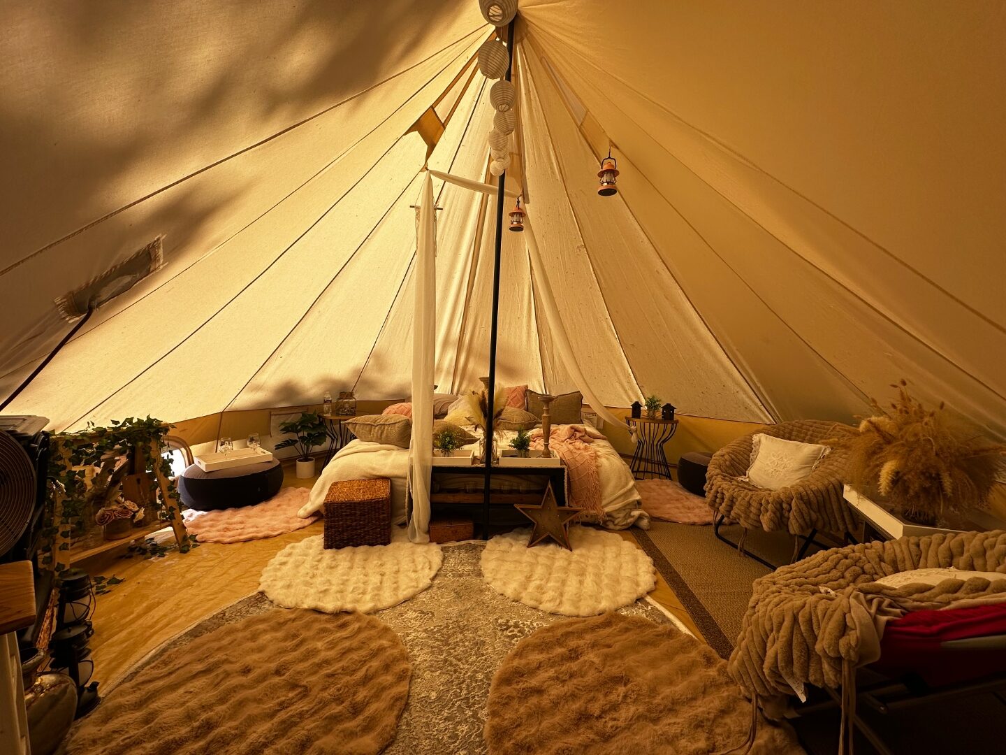 Luxury canvas bell tent interior with full styling — bed, canopy, chairs, rugs, lanterns and pampas.