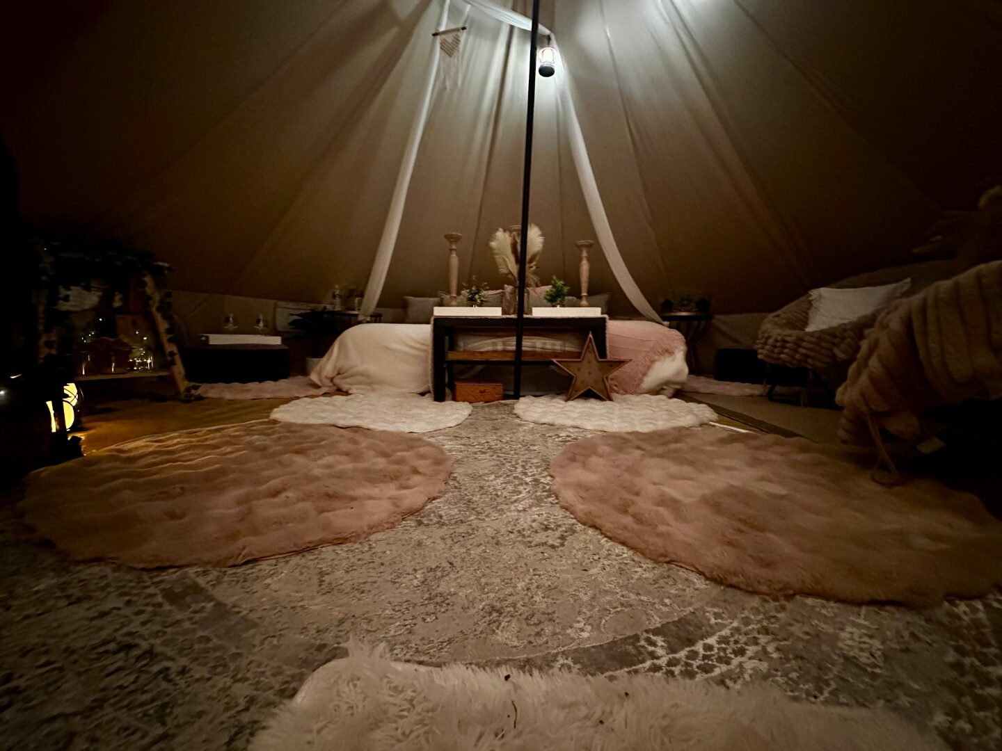 Wide bell tent interior with layered rugs, wooden star marquee and pampas styling.